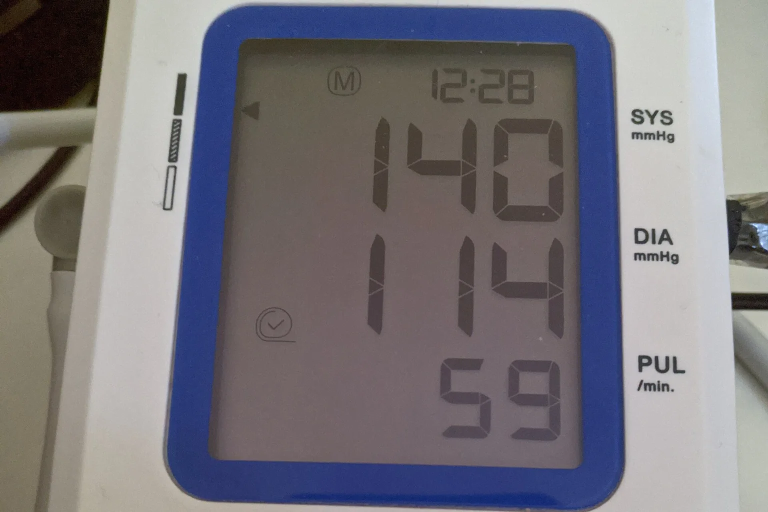 Close-up of a digital blood pressure monitor screen showing 140 systolic, 114 diastolic and a pulse of 59