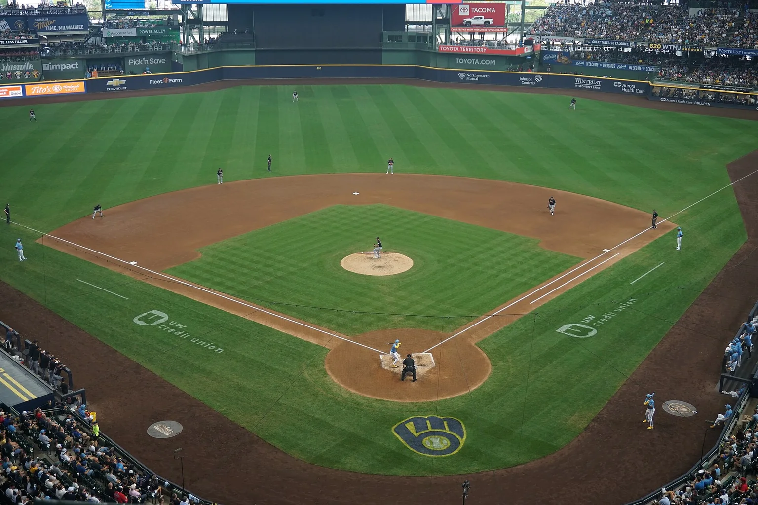 Aerial view of a baseball game at American Family Field with the Brewers logo mowed into the grass behind home plate