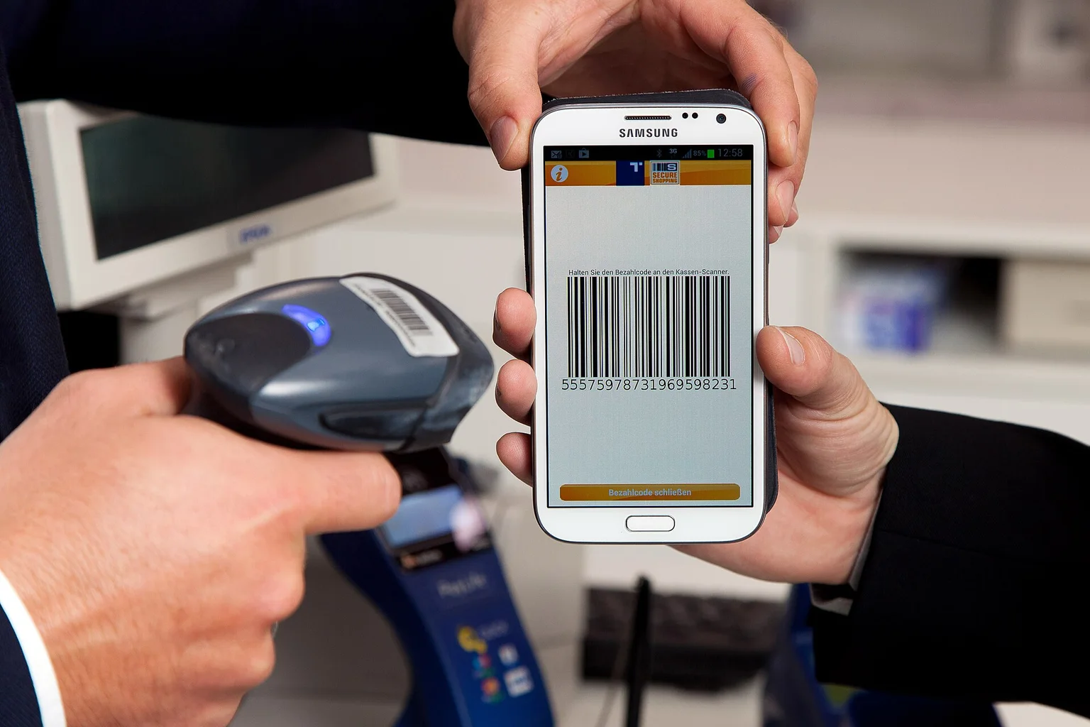 Hands holding a Samsung smartphone showing a payment barcode to a handheld checkout scanner