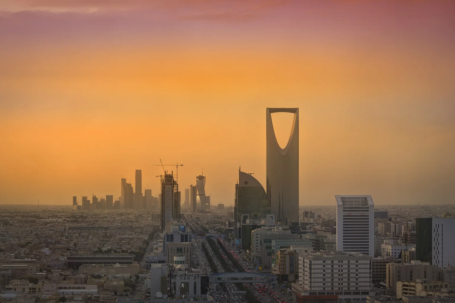 Skyline of Riyadh at sunset, with the Kingdom Tower rising above the city and towers in the distance.