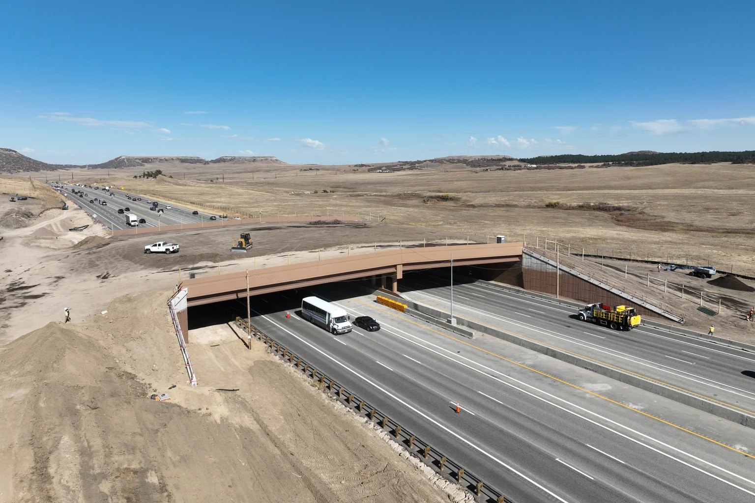 Aerial view of the Greenland Wildlife Overpass, a wide earth-covered bridge spanning Interstate 25 in open Colorado grassland, with traffic passing beneath.