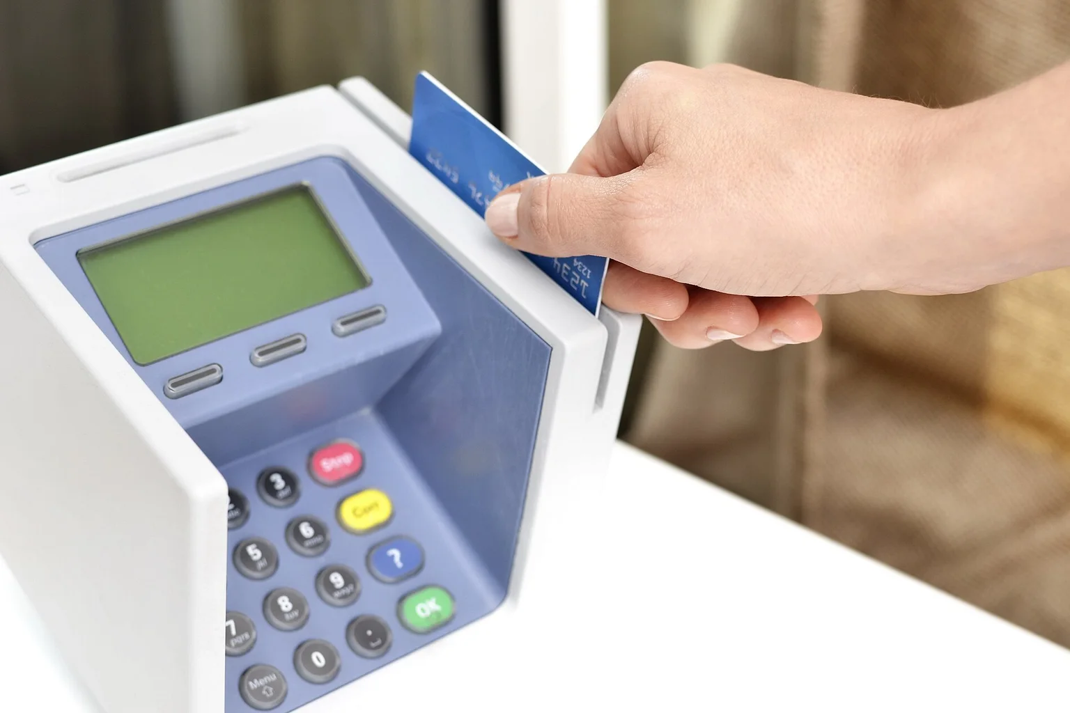 A hand sliding a blue credit card through a point-of-sale card reader.