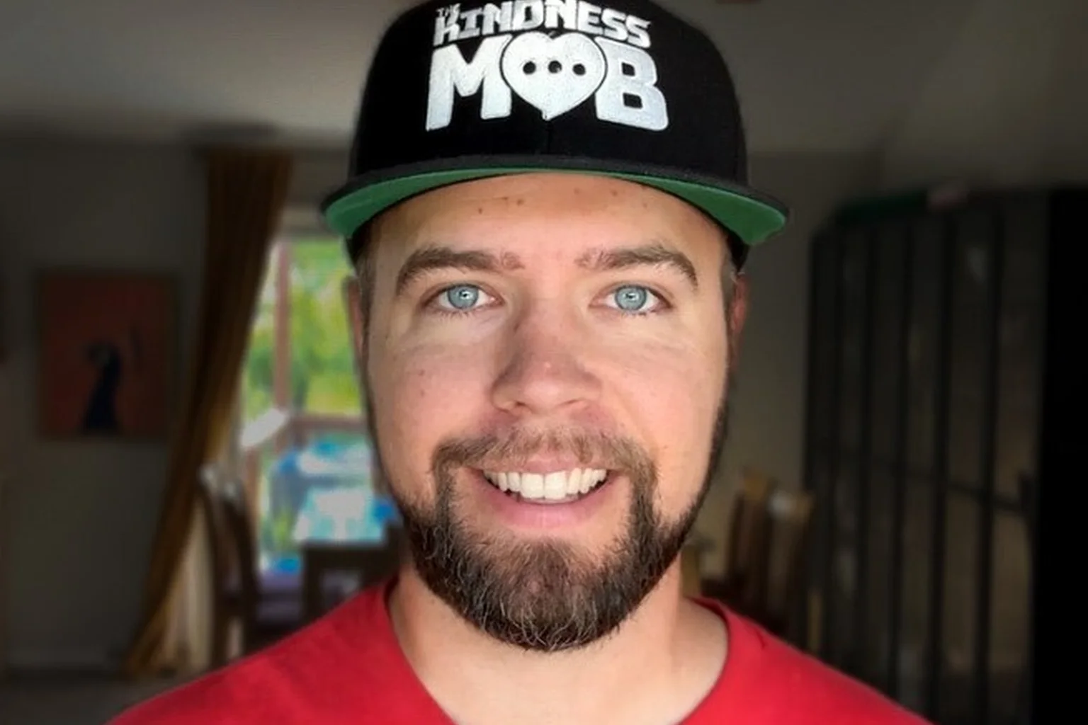 Tyler Brickley, founder of The Kindness Mob, smiling in a Kindness Mob cap and red Kindness T-shirt.
