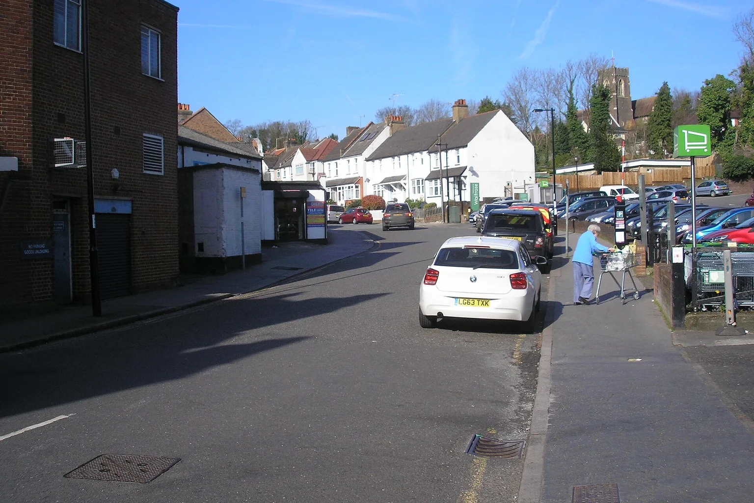 Malcolm Road in Coulsdon, a sloping street with terraced houses, parked cars and a church tower on the hill behind