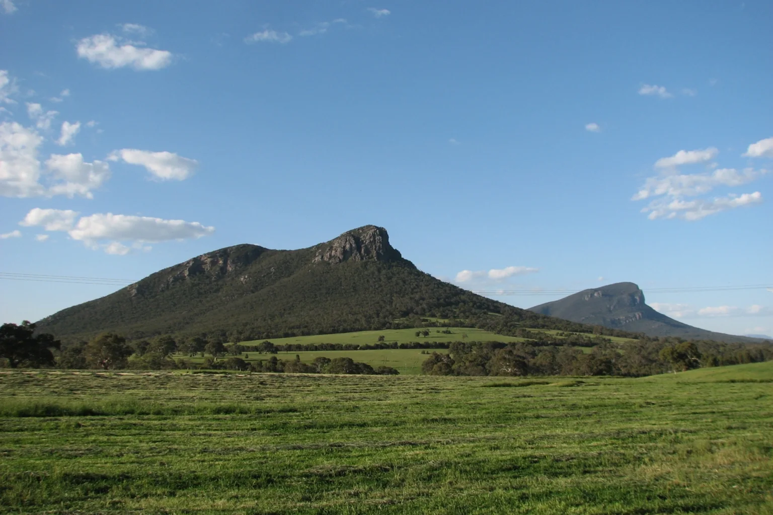 Two rocky mountains, Mount Sturgeon and Mount Abrupt, rising above green paddocks under a blue sky near Dunkeld, Victoria