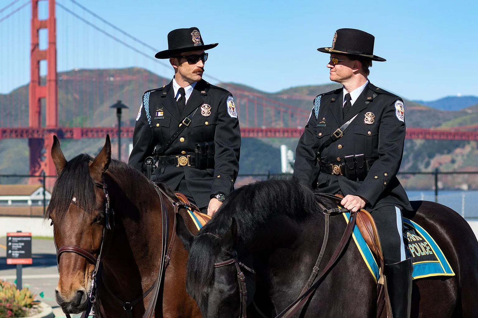 Two uniformed mounted police officers on dark horses, with the Golden Gate Bridge in the background.