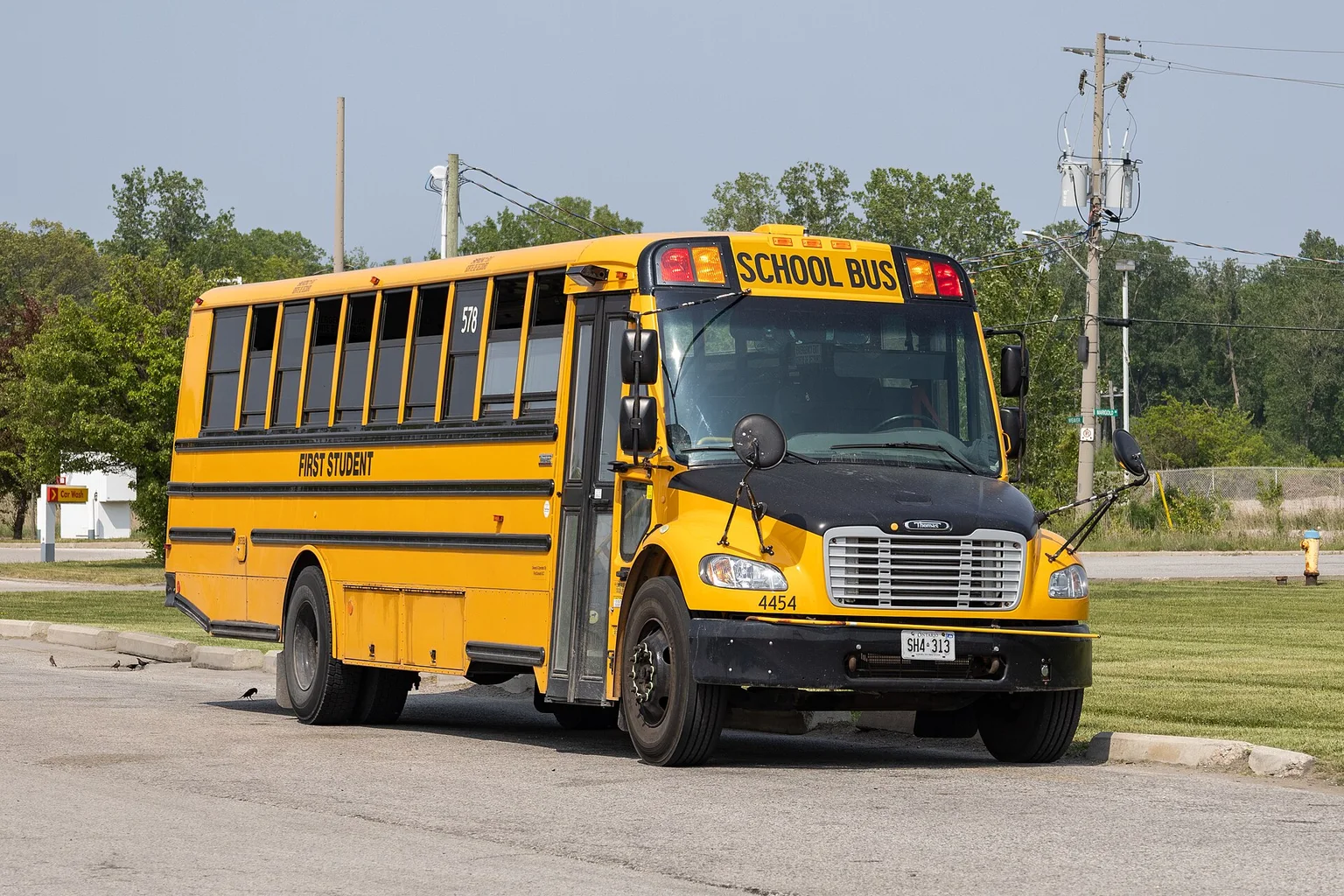 A yellow school bus with its door closed, parked on pavement beside grass and trees.