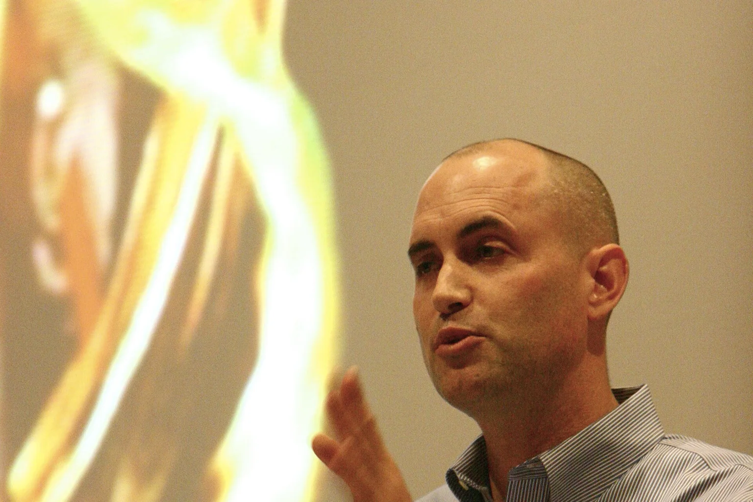 BJ Fogg, a bald man in a striped button-up shirt, gestures with one hand while speaking at a wooden podium with a microphone.