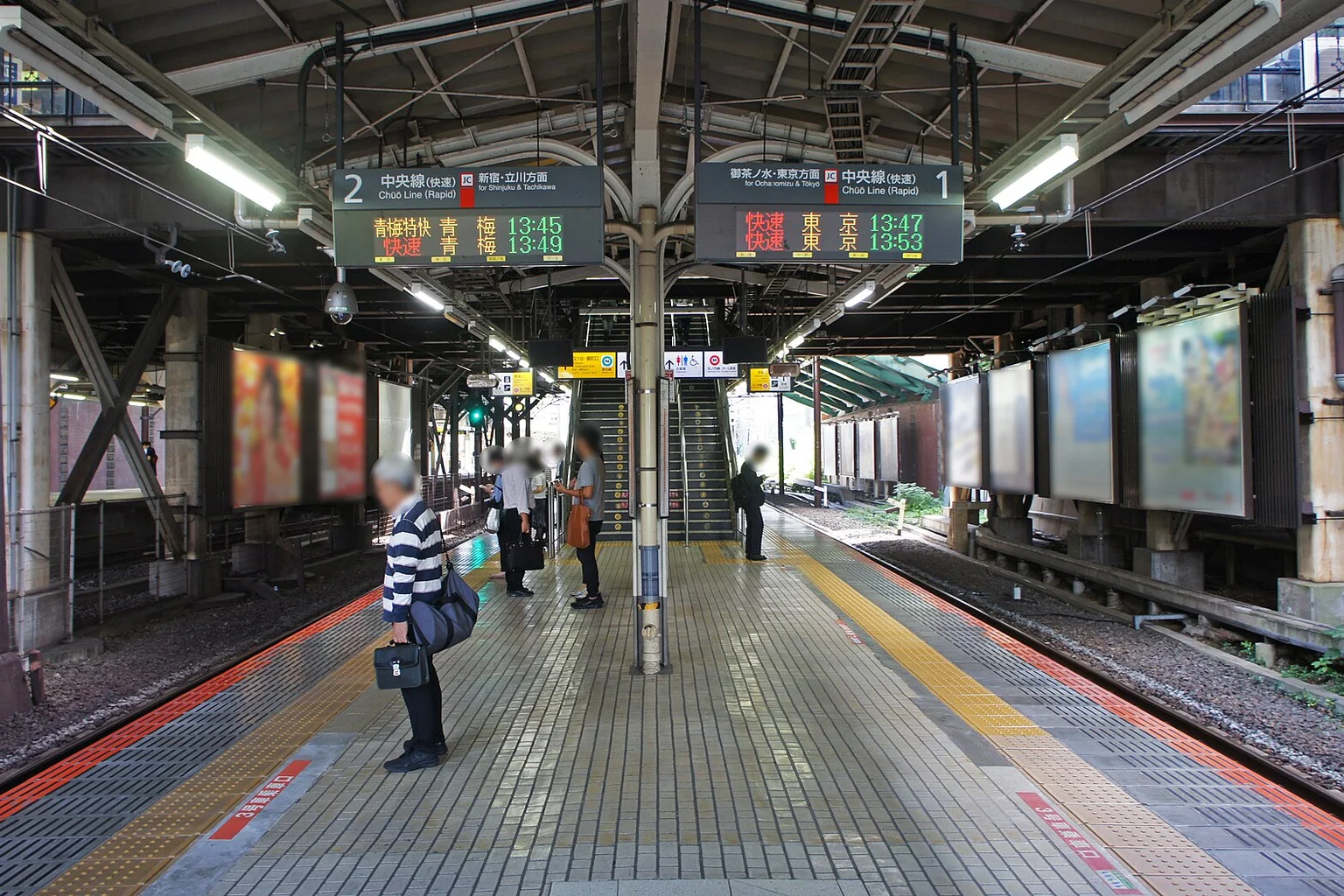 Commuter platform at Yotsuya Station in Tokyo with overhead departure displays and passengers waiting.