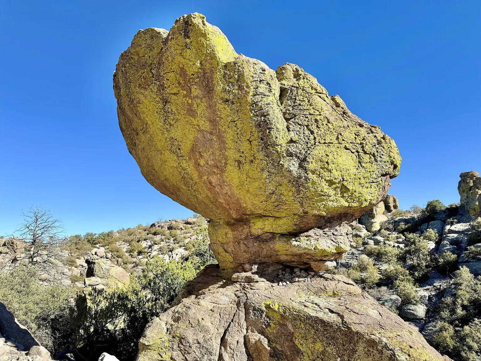 A huge lichen-covered boulder balanced on a narrow base against a bright blue sky.