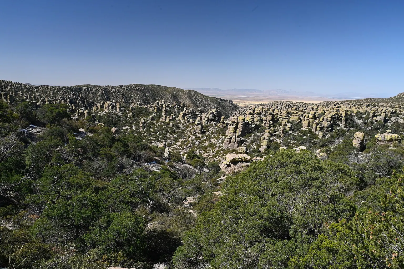 A wide view over green hills and rock spires, stretching to a distant valley.