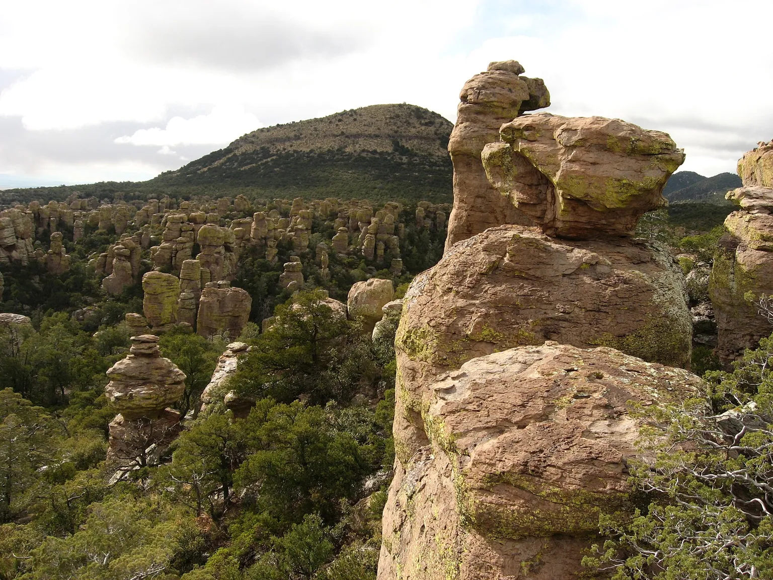 A stack of balanced rock in the foreground, with a forest of rock spires and a rounded peak behind it.